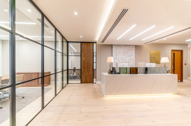 Modern office reception with sleek marble desk, glass partitions, and integrated lighting design