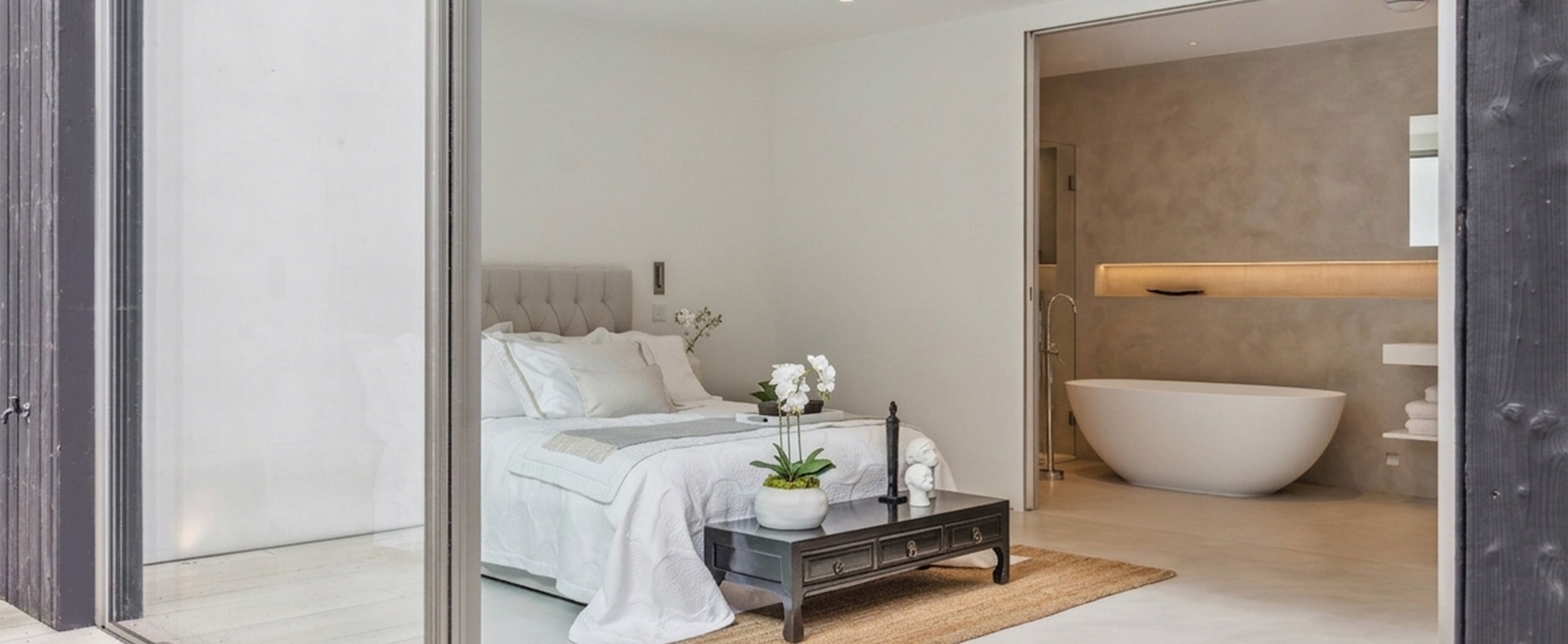 Luxury bedroom with modern lighting design and integrated tech, featuring a freestanding bathtub and minimalist decor.