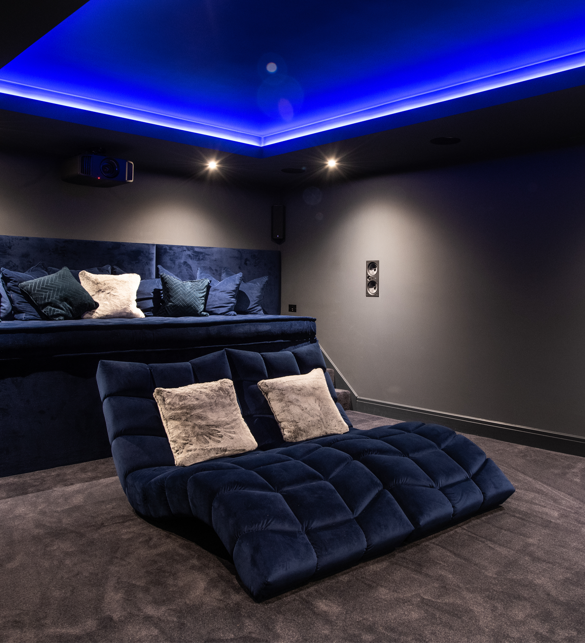 Luxury home cinema with blue ambient lighting, plush velvet seating, and integrated audio visual system