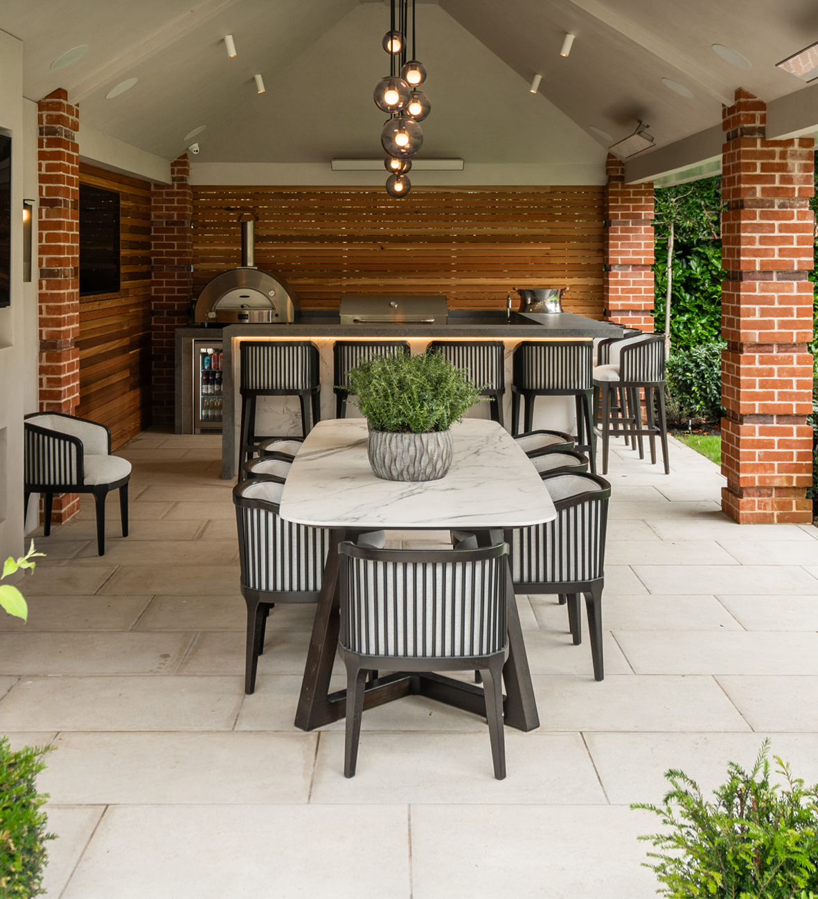 Luxury outdoor kitchen with marble dining table, modern lighting, and integrated appliances under covered patio