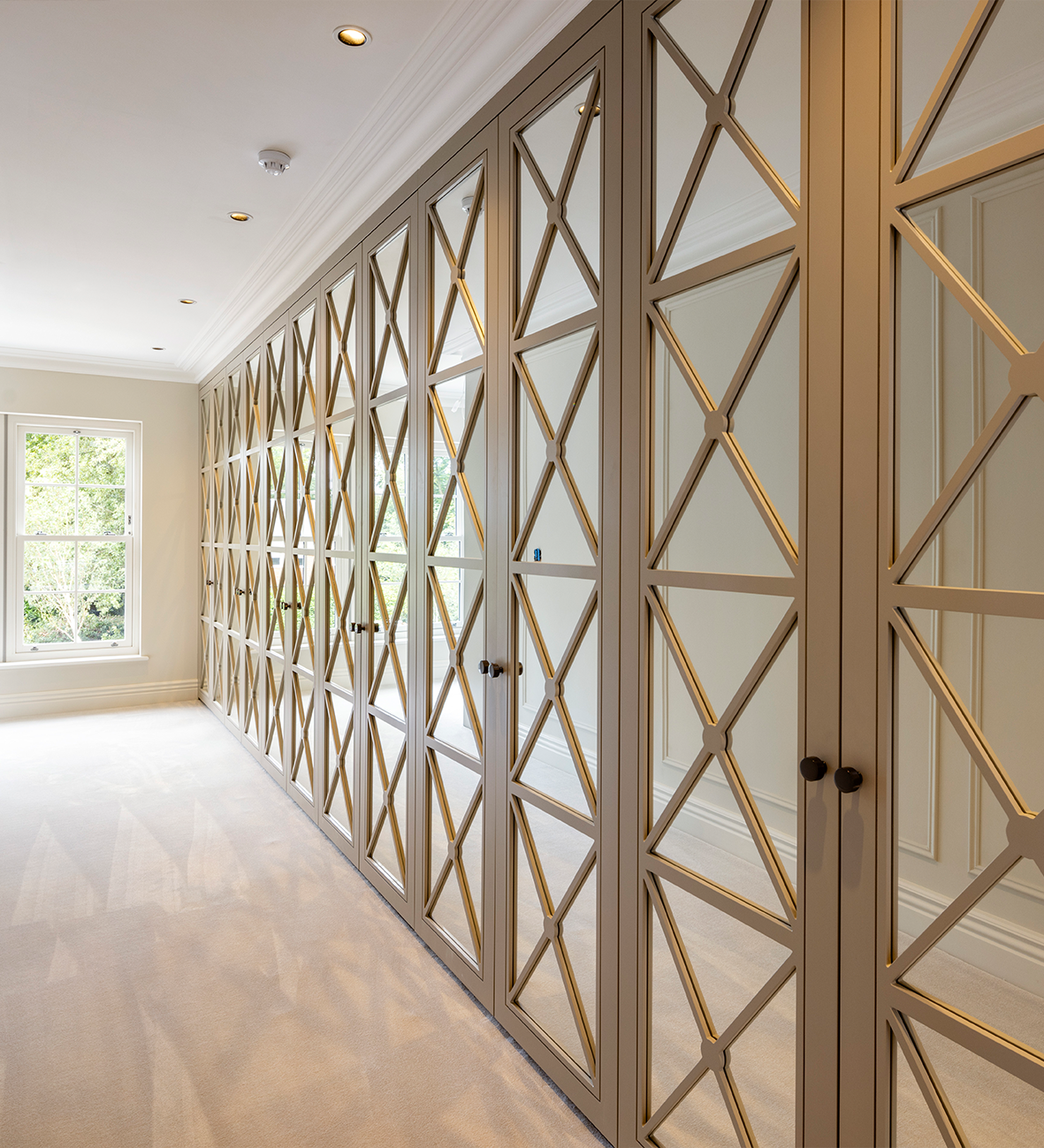 Luxury built-in wardrobe with geometric glass panel doors, recessed lighting, and elegant interior design